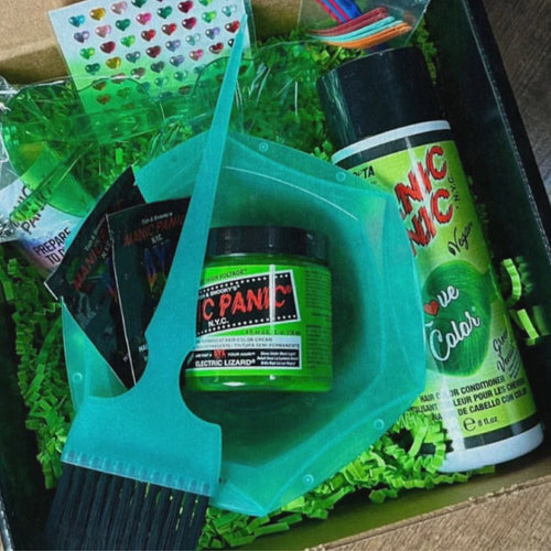 A hair dye kit in a cardboard box filled with green paper shred, including a jar of green 'Electric Lime' hair dye, a large teal plastic scoop, a can of 'Panic Panic' dye, a black brush, and a sheet of heart-shaped stickers.