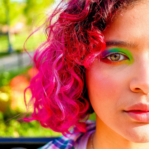Close-up of a person with vibrant pink hair and colorful makeup outdoors.